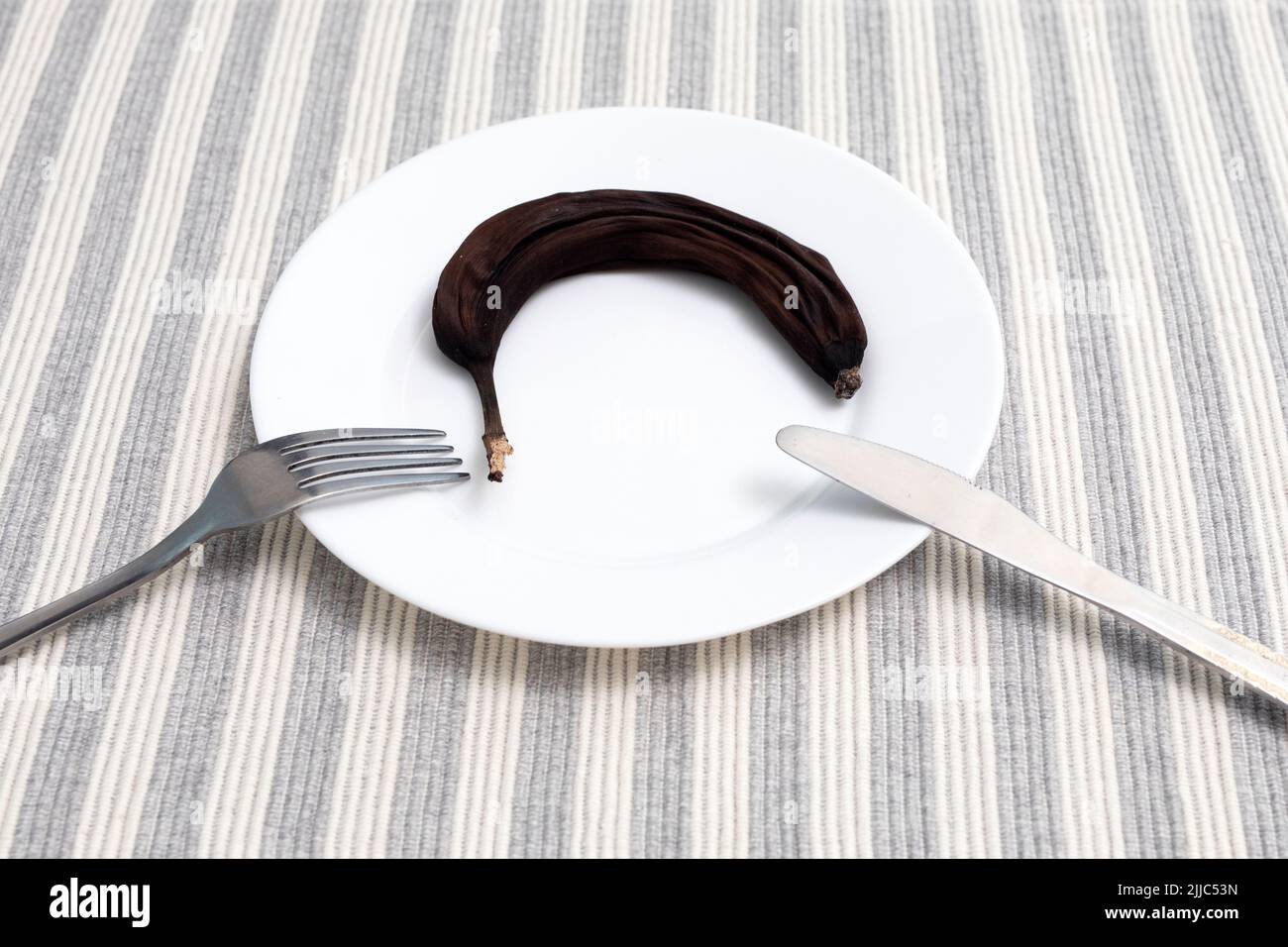 Banana essiccata in piastra bianca con forchetta e coltello. Frutta secca. Snack sano. Foto Stock