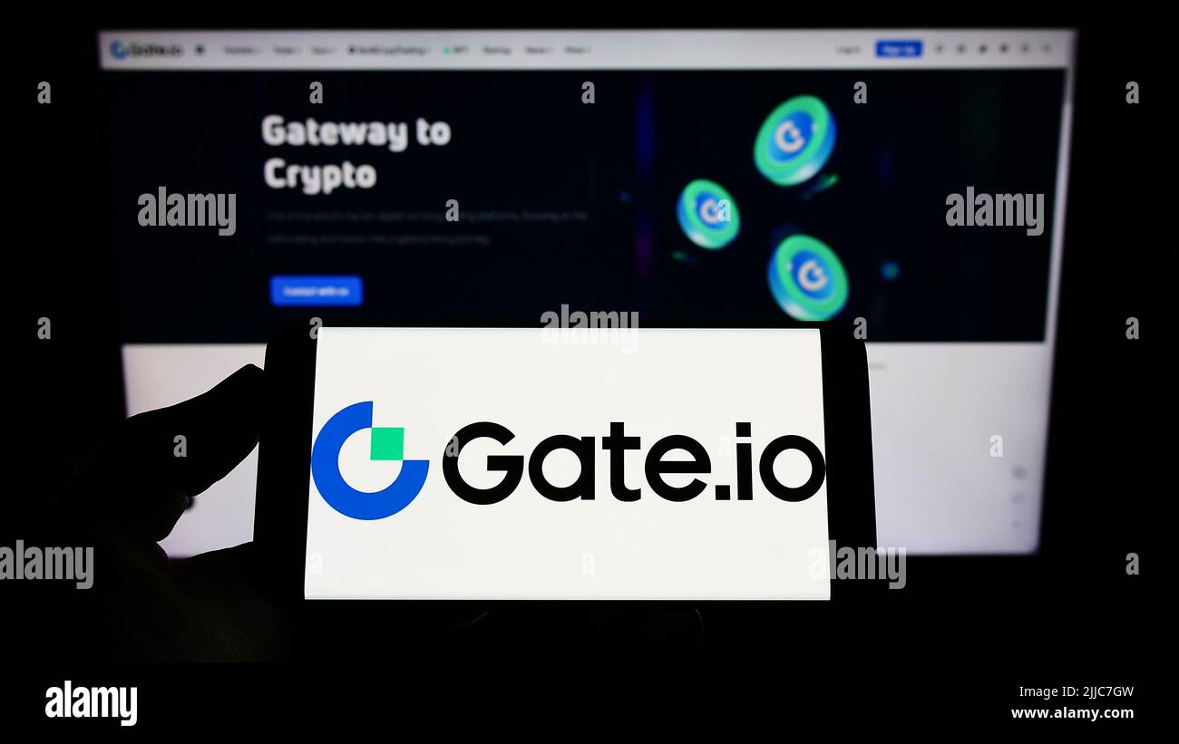 Persona che tiene lo smartphone con il logo della società di scambio cripto Gate Global Corp. Sullo schermo di fronte al sito web. Mettere a fuoco sul display del telefono. Foto Stock