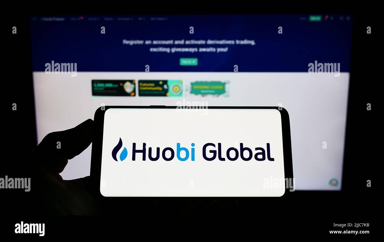 Persona che tiene lo smartphone con il logo della società di scambio criptato Huobi Global sullo schermo di fronte al sito web. Mettere a fuoco sul display del telefono. Foto Stock