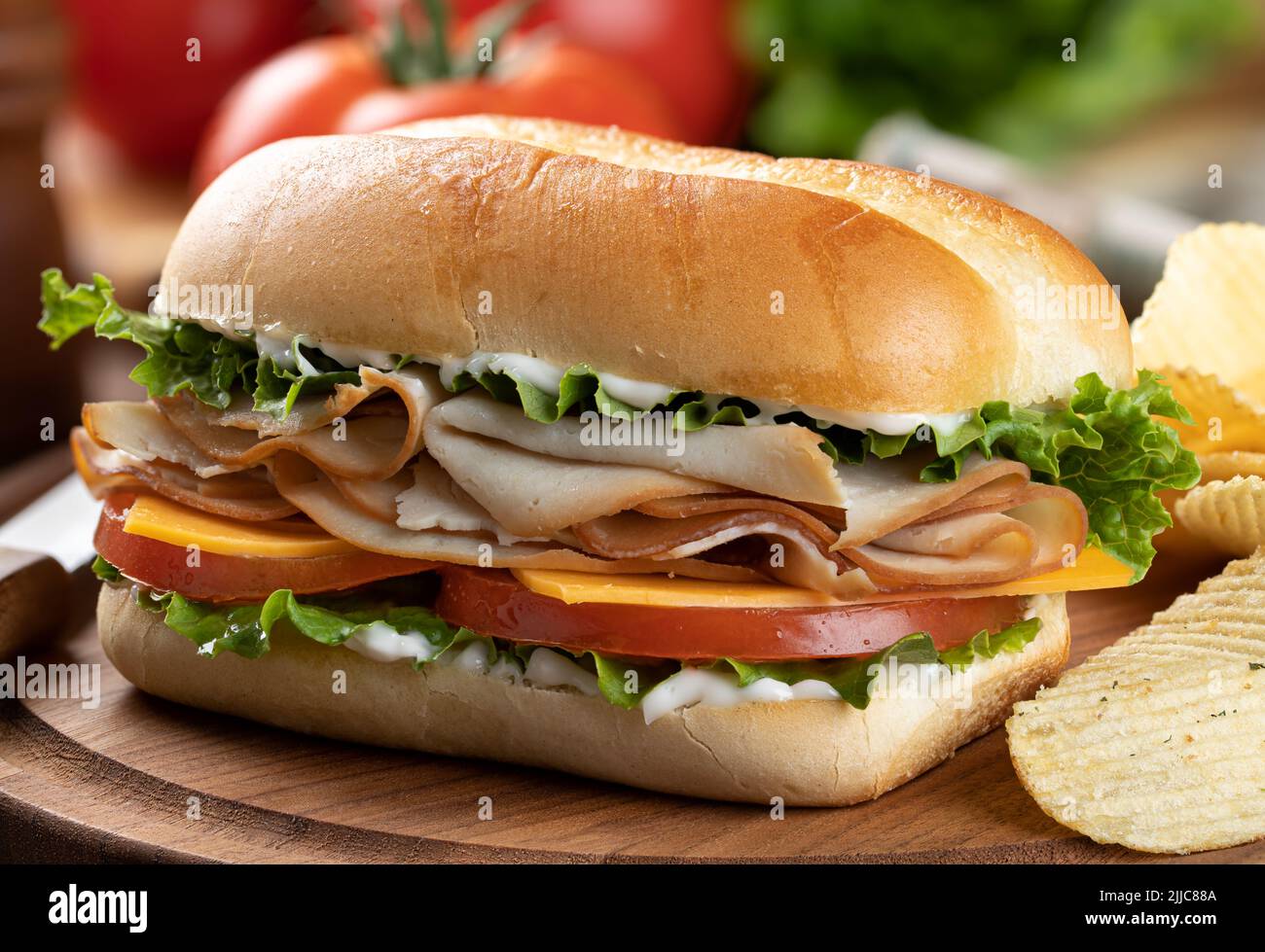 Sandwich sottomarino a base di tacchino, formaggio, lattuga, pomodoro e maionese con patatine fritte su un piatto di legno Foto Stock