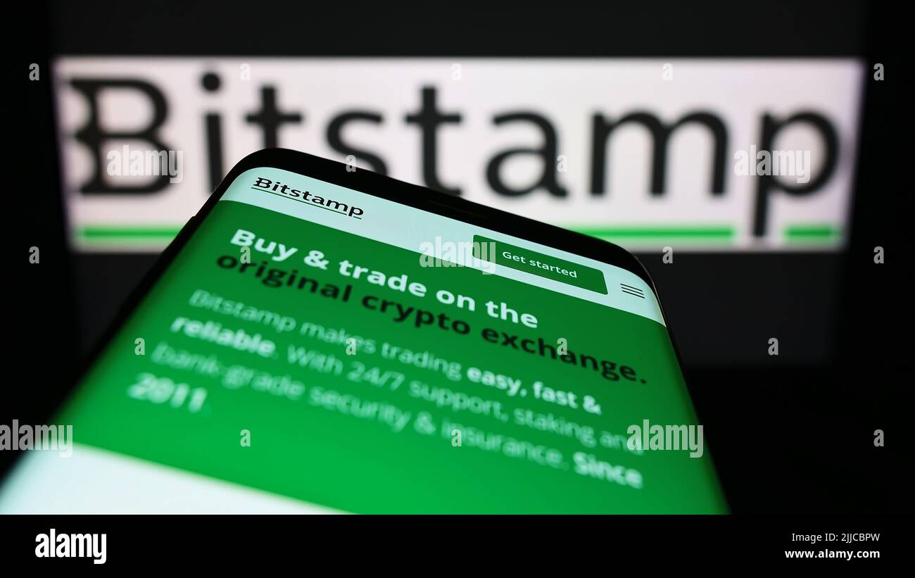 Telefono cellulare con sito web della società di scambio criptovaluta Bitstamp Ltd. Sullo schermo di fronte al logo aziendale. Mettere a fuoco sulla parte superiore sinistra del display del telefono. Foto Stock