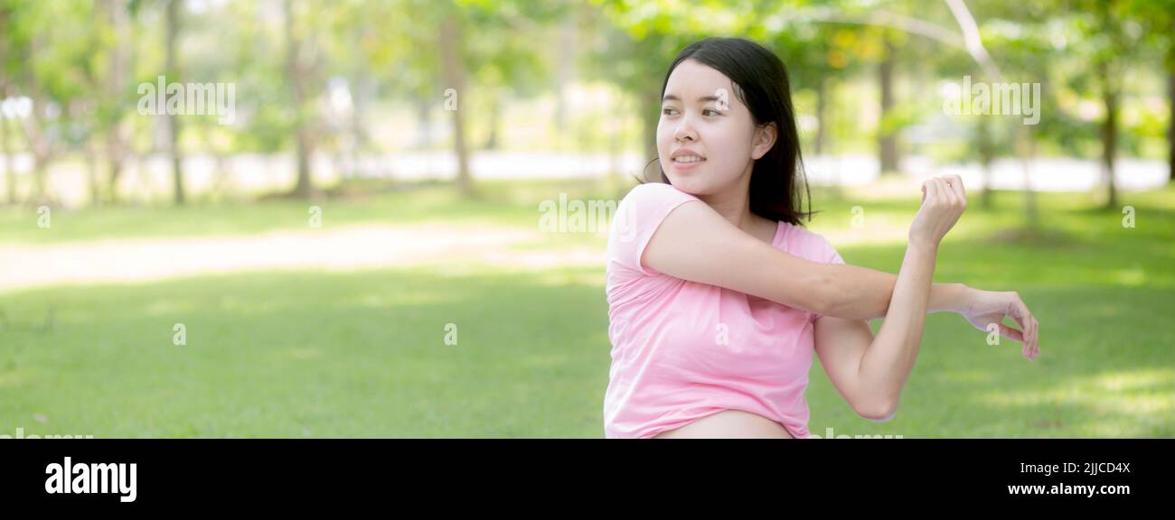Felicità giovane donna asiatica incinta seduta facendo esercizio sportivo con mani stretch muscolo per la salute al parco, madre che pratica yoga per il leisur Foto Stock