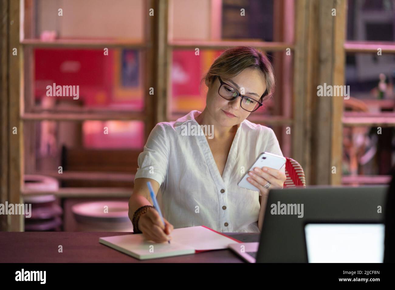 Tutor di lingua donna focalizzato che guarda lo smartphone scrivere note, preparandosi per la lezione virtuale Foto Stock