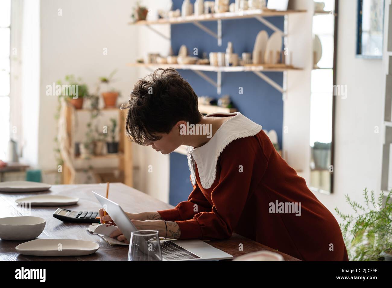 Focalizzato artigiano donna proprietario negozio di ceramica facendo contabilità, misurando la redditività delle piccole imprese Foto Stock