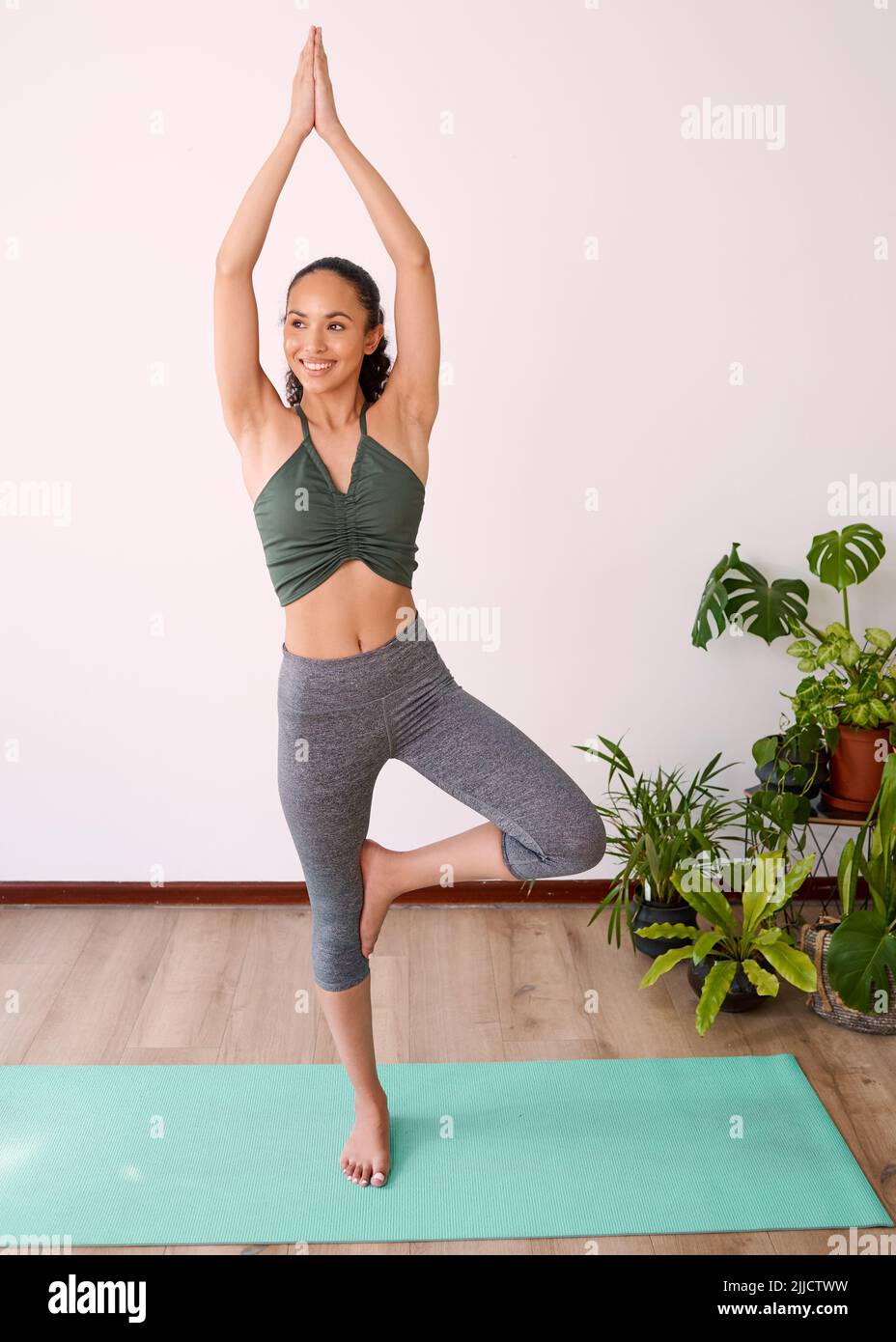 Una giovane donna attraente sorride mentre si esibisce albero posa alla pratica di yoga Foto Stock