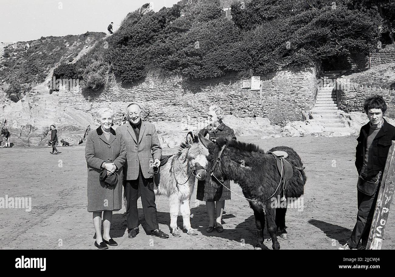 1970s, storico, persone in piedi per la loro foto accanto a noleggiare asini su una spiaggia, Inghilterra, Regno Unito. Il ragazzo che assume gli asini è in piedi lì. Foto Stock