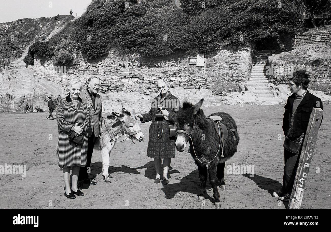 1970s, storico, persone in piedi per la loro foto accanto a noleggiare asini su una spiaggia, Inghilterra, Regno Unito. Il ragazzo che assume gli asini è in piedi lì. Foto Stock