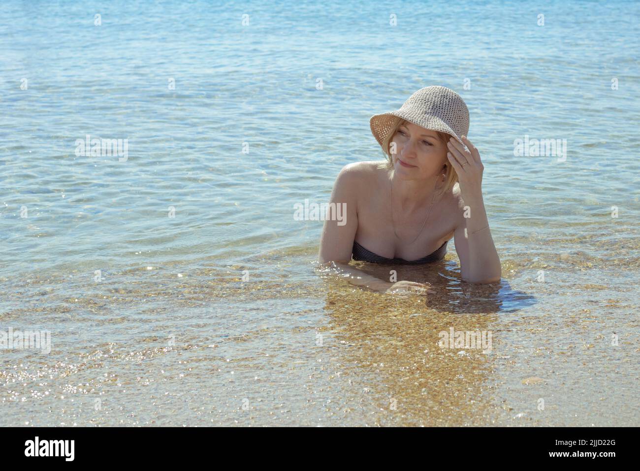 Una donna adulta in costume da bagno si trova in acqua di mare. Vacanze estive sulla costa del mare. Foto Stock