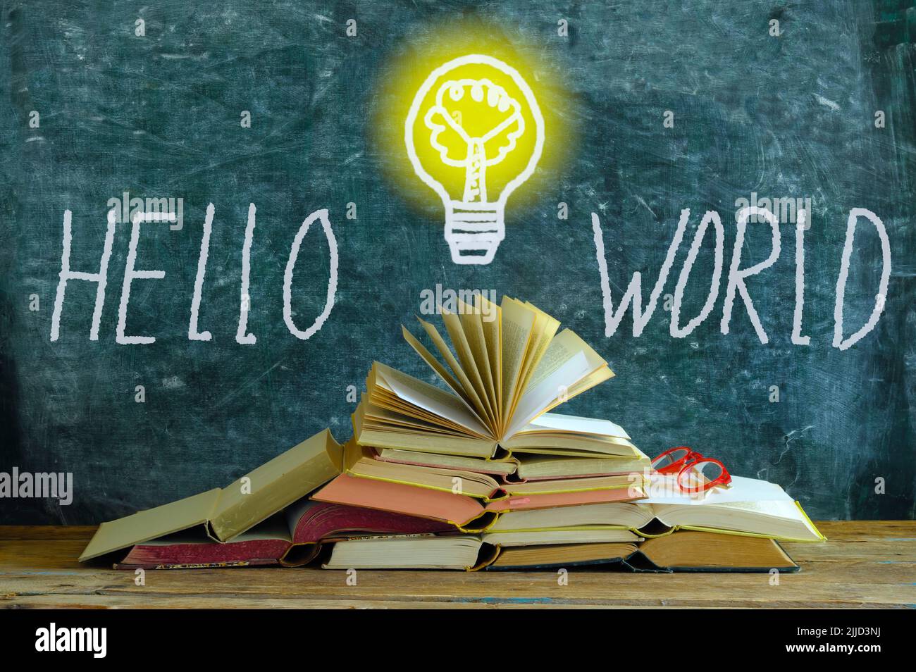 pila di libri di fronte a una lavagna, disegno di una lampadina e slogan hello mondo, conoscenza, istruzione e concetto di integrazione sociale Foto Stock