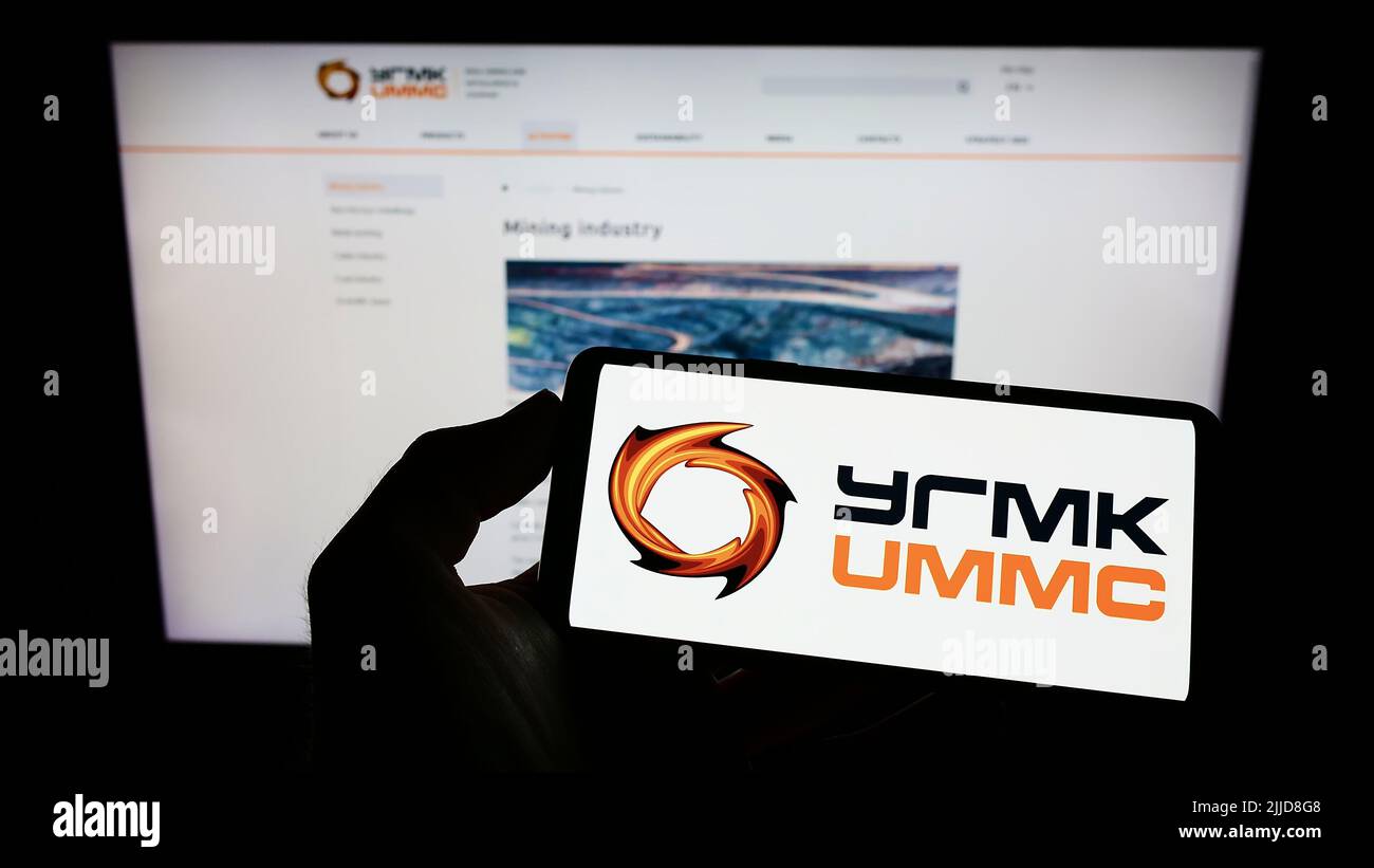 Persona che tiene il telefono cellulare con il logo di Ural Mining and Metallurgical Company (UMMC) sullo schermo di fronte alla pagina web. Mettere a fuoco sul display del telefono. Foto Stock