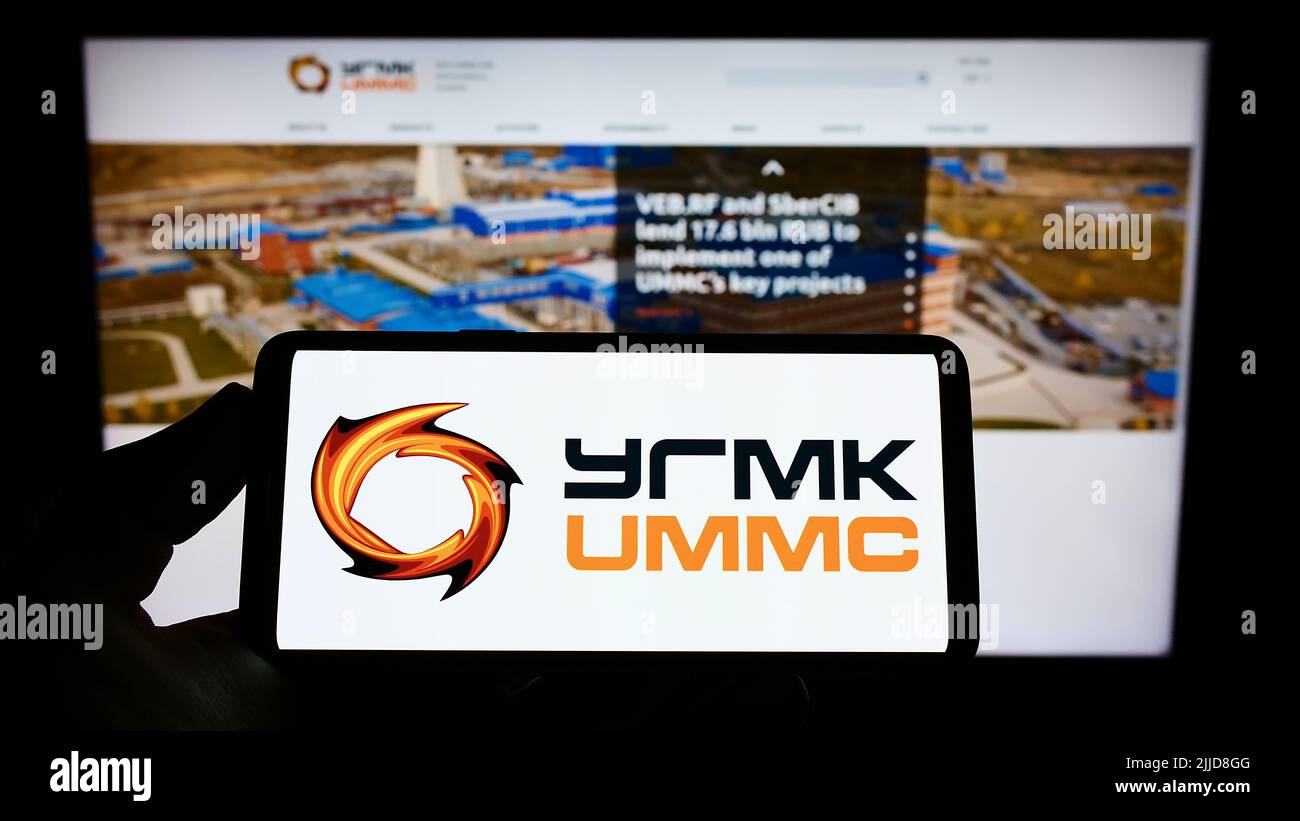 Persona che tiene il cellulare con il logo di Ural Mining e Metallurgical Company (UMMC) sullo schermo di fronte al sito web aziendale. Mettere a fuoco sul display del telefono. Foto Stock