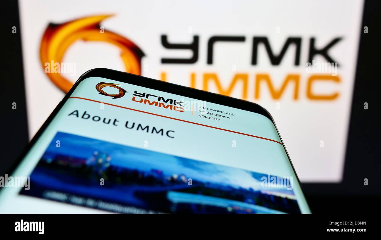 Telefono cellulare con sito web della Ural Mining and Metallurgical Company (UMMC) sullo schermo di fronte al logo aziendale. Mettere a fuoco sulla parte superiore sinistra del display del telefono. Foto Stock