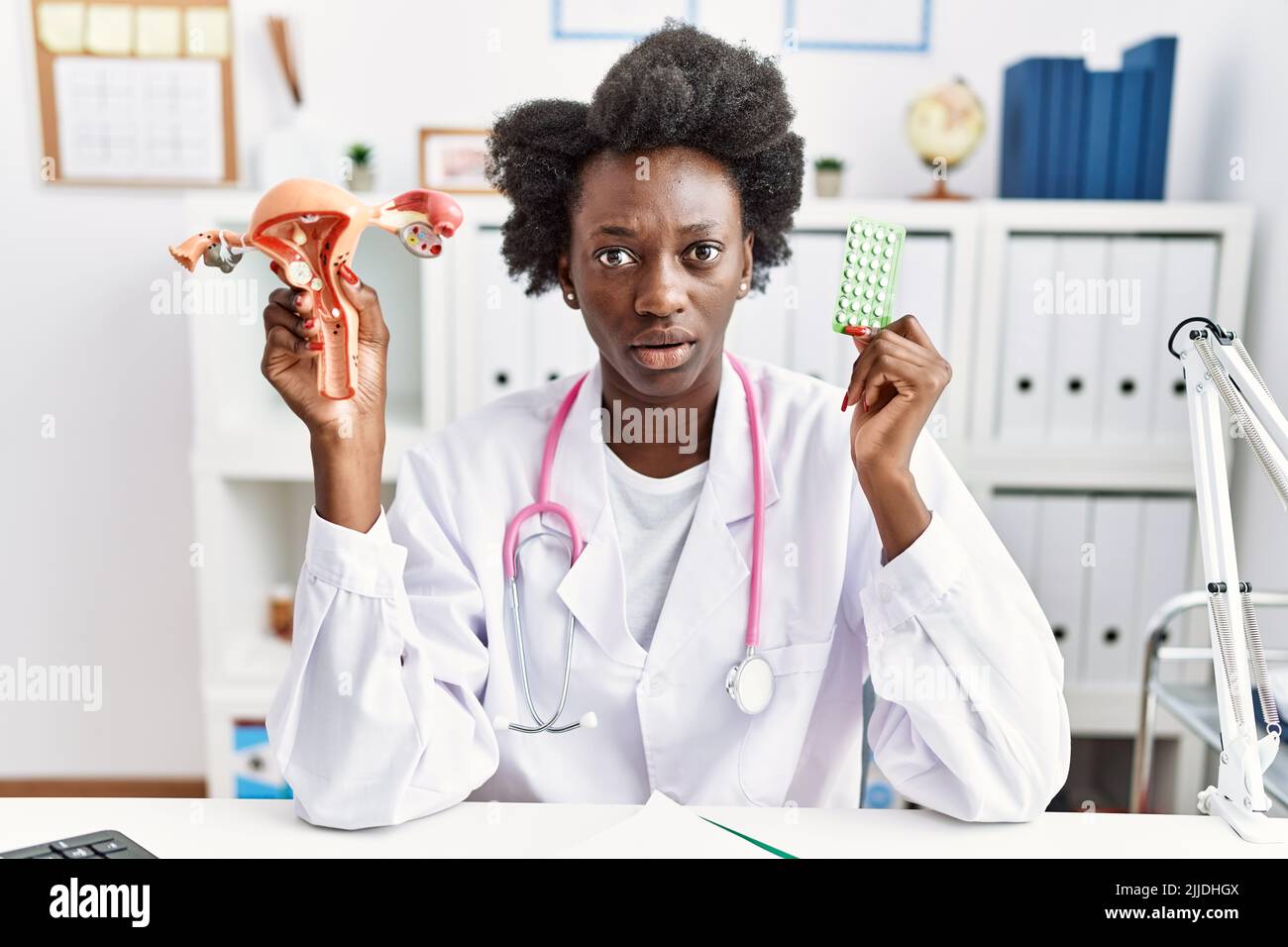 Medico africano donna che tiene anatomico organo genitale femminile e pillole di controllo delle nascite clueless e confuso espressione. Concetto di dubbio. Foto Stock