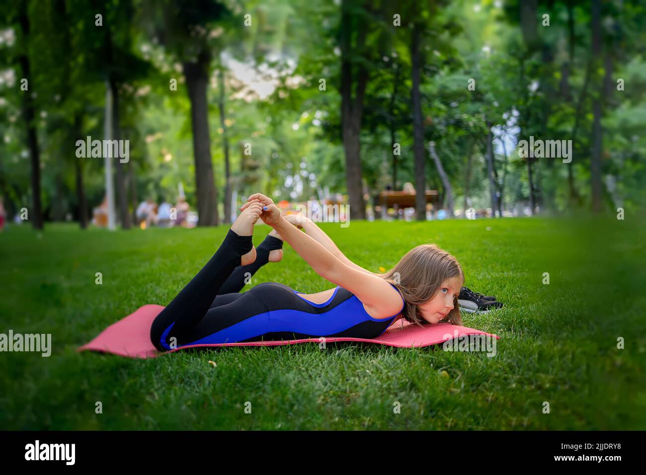 nel parco, una bambina si piega indietro, si aggrappa le gambe, esegue gli elementi yoga, si allunga Foto Stock