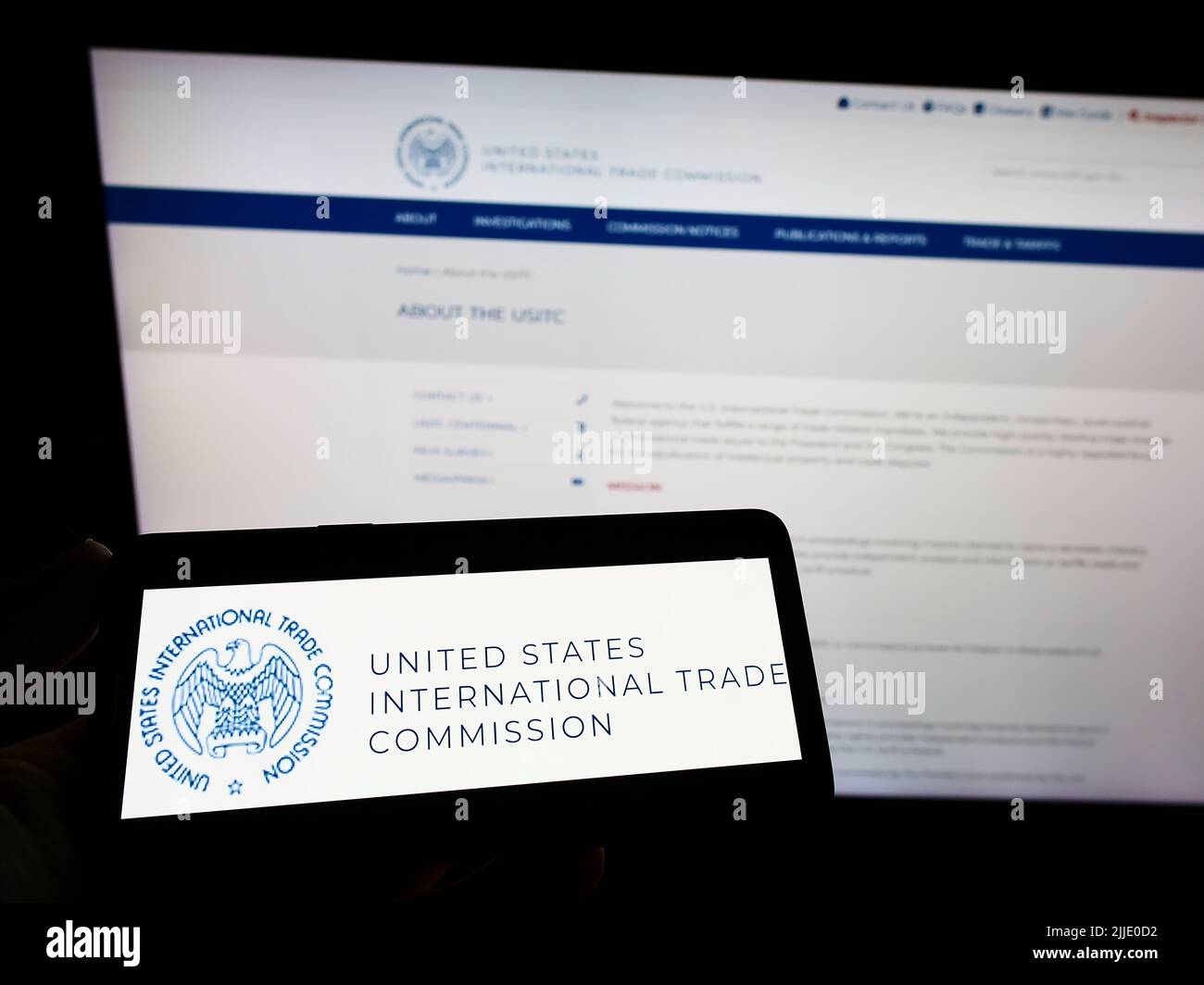 Persona che tiene uno smartphone con il logo della US International Trade Commission (USITC) sullo schermo di fronte al sito Web. Mettere a fuoco sul display del telefono. Foto Stock