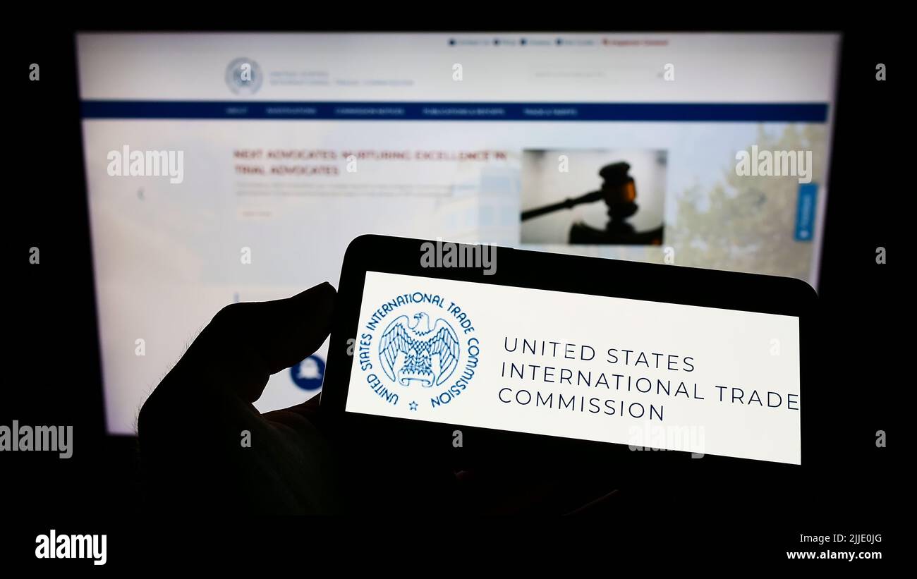 Persona che tiene il cellulare con il logo della American International Trade Commission (USITC) sullo schermo di fronte alla pagina web. Mettere a fuoco sul display del telefono. Foto Stock