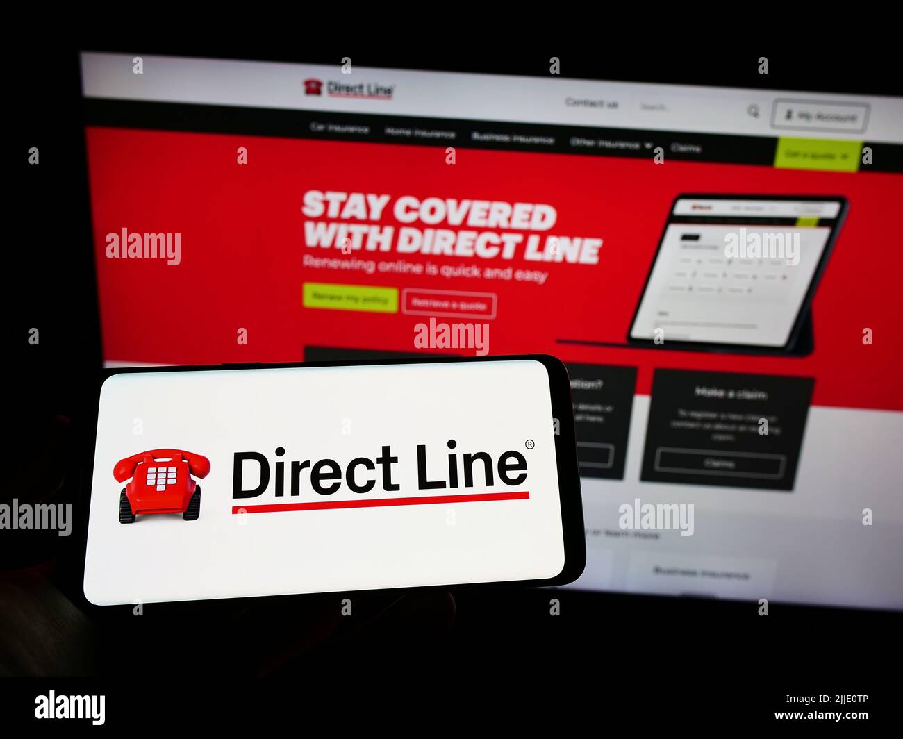 Persona che detiene il telefono cellulare con il logo della società U K Insurance Limited (linea diretta) sullo schermo di fronte alla pagina web. Mettere a fuoco sul display del telefono. Foto Stock