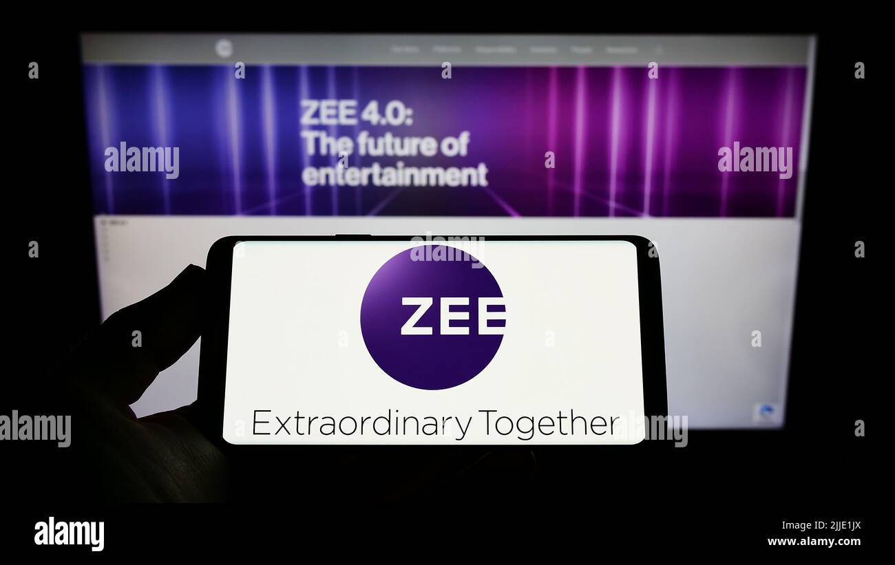 Persona che tiene uno smartphone con il logo della società Zee Entertainment Enterprises Limited sullo schermo di fronte al sito Web. Mettere a fuoco sul display del telefono. Foto Stock