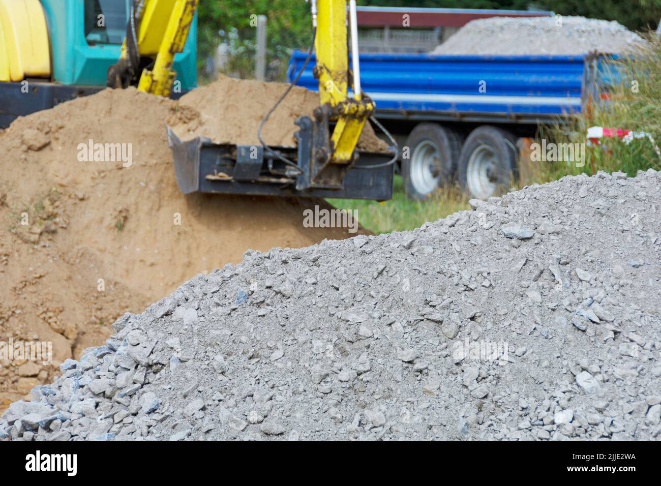 Sostituzione del terreno - escavatore con benna completa e cumulo di rocce frantumate in primo piano Foto Stock