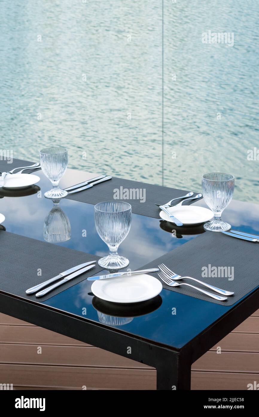 Bicchieri vuoti di cristallo, piatti bianchi e posate su un tavolo in un ristorante sulla spiaggia. Tavolo per una cena di festa. Foto Stock