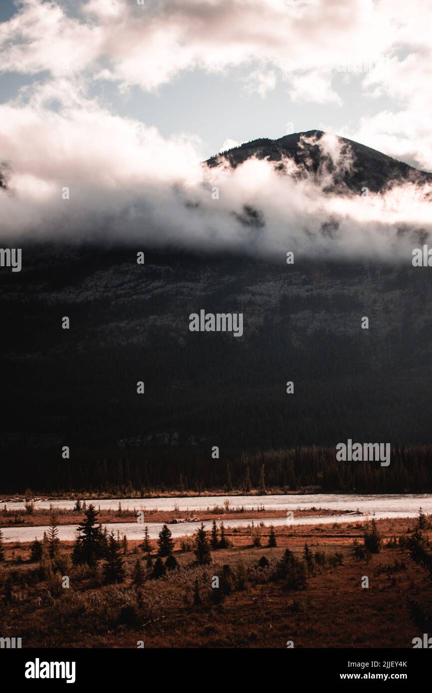 Una montagna alta e imponente che si affaccia su un fiume e foresta. È così alto che raggiunge anche sopra alcune nuvole. Foto Stock
