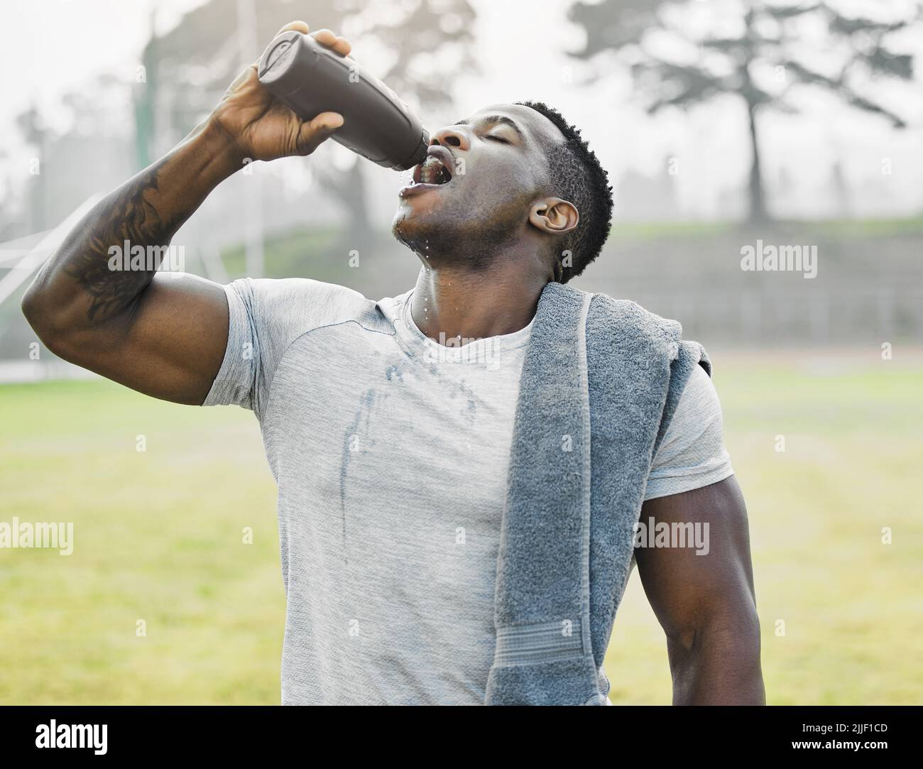 È il momento di rinfrescarsi. Un bel giovane atleta maschile beve acqua mentre si esercita all'esterno. Foto Stock