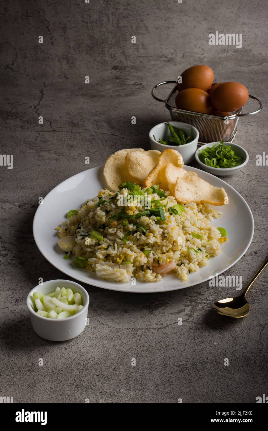 Riso fritto o nasi goreng kampung, con uova strapazzate, cipolla primaverile e cracker su piatto bianco Foto Stock