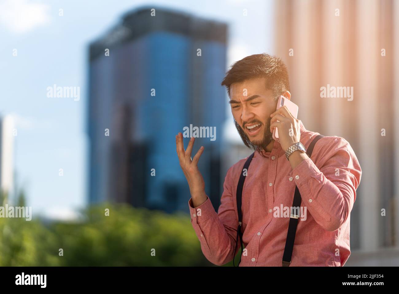 Un uomo d'affari asiatico che parla sul suo cellulare con rabbia Foto Stock