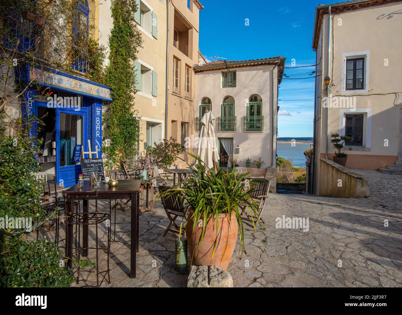 Gruissan, Francia - 20 febbraio 2022: Una piazza nel vecchio villaggio di Gruissan, Francia meridionale, con un caffè e un varco che si aprono su di un lago, Tak Foto Stock