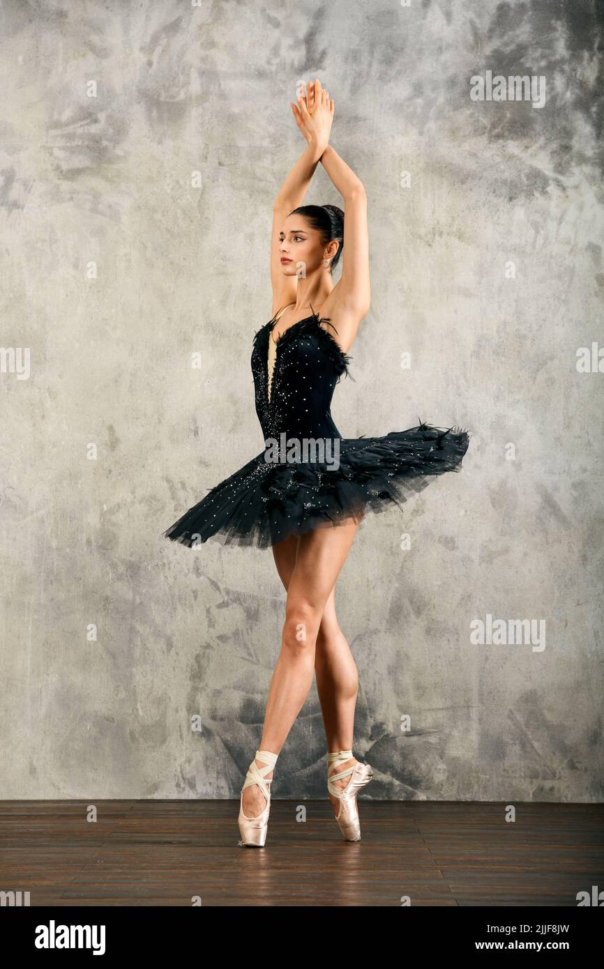 Corpo pieno di danza balletto femminile aggraziata in costume di cigno nero in pointe in piedi su tittoes con le braccia sollevate durante le prove Foto Stock