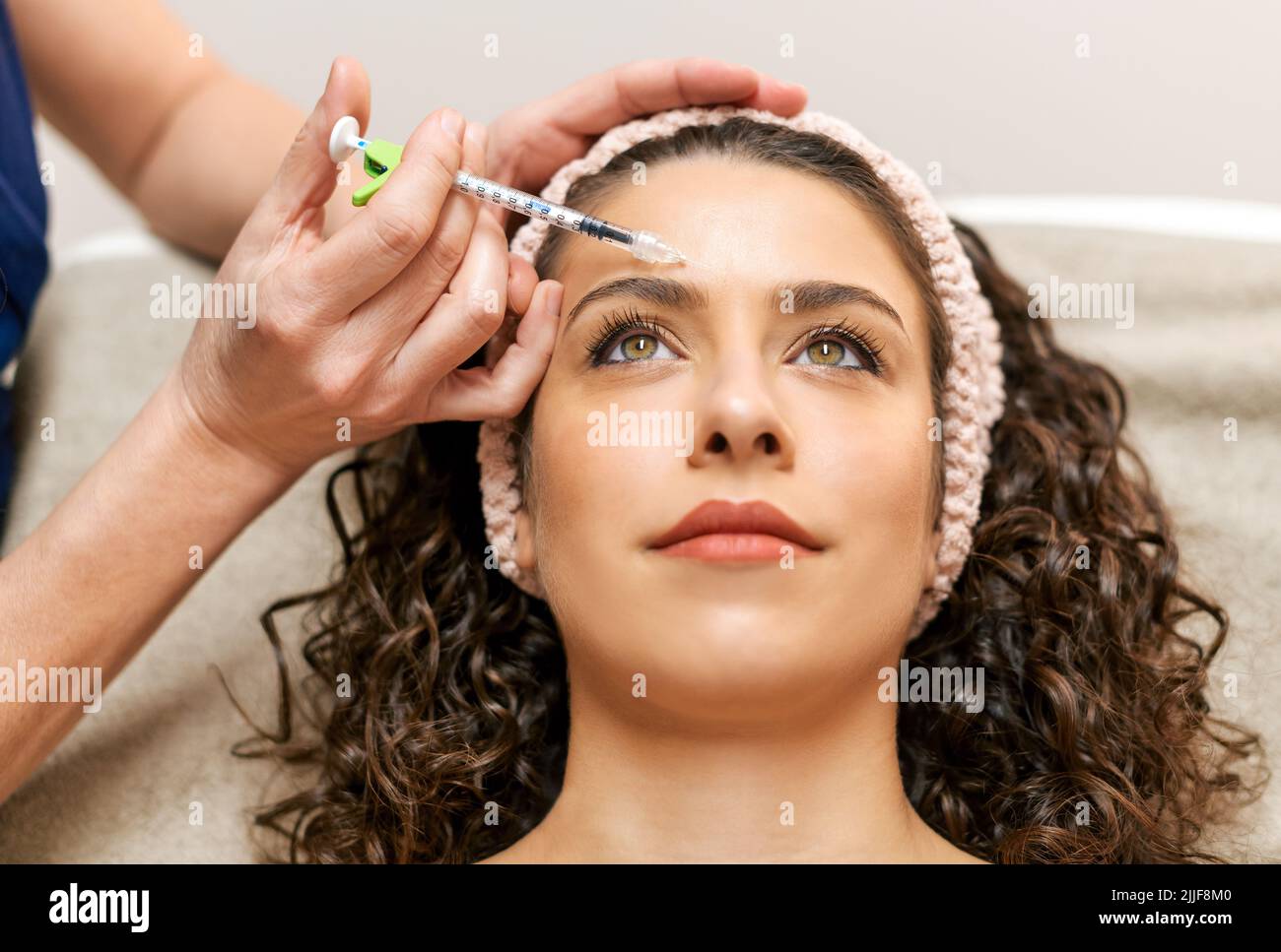 Raccolto anonimo estetista iniezione affascinante cliente femminile con anti età riempitivo durante la procedura di cura della pelle in moderno salone di bellezza luce Foto Stock