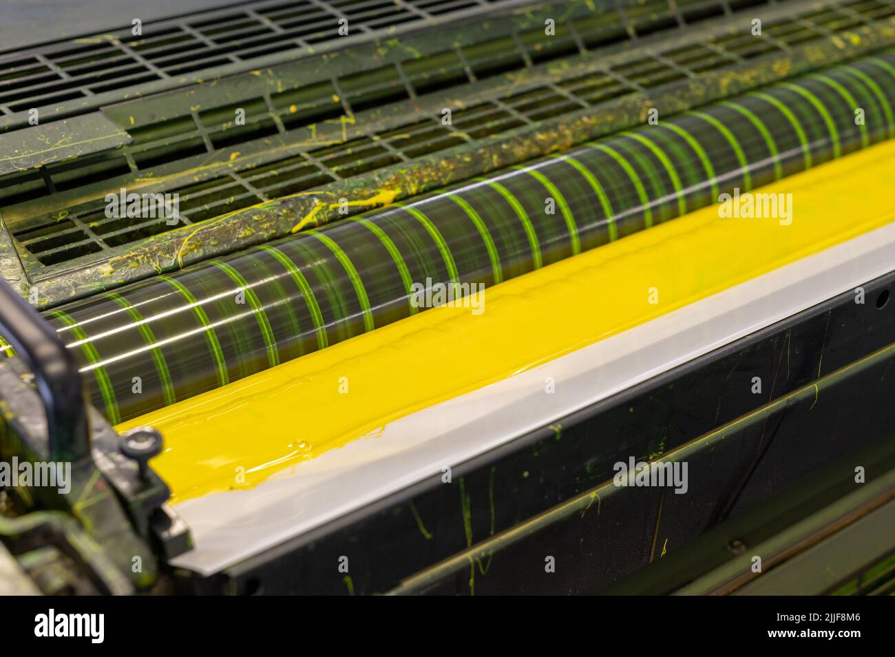 Da sopra striscia di inchiostro giallo brillante diffusa all'interno di una stampante offset industriale in officina tipografica Foto Stock