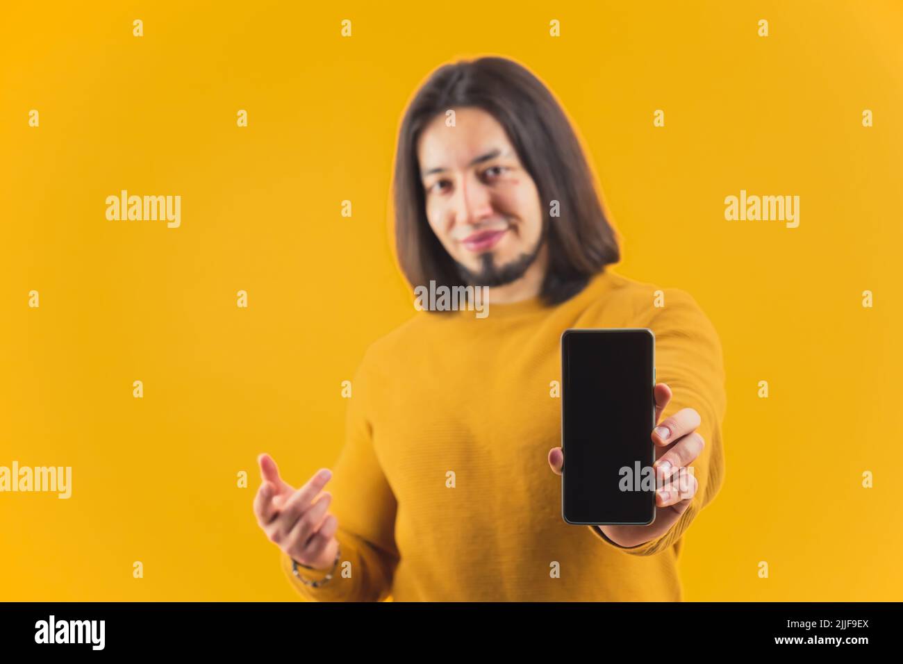 Una giovane persona ispanica bearded che fa pubblicità ad un telefono visualizzato su uno sfondo giallo dello studio. Foto di alta qualità Foto Stock