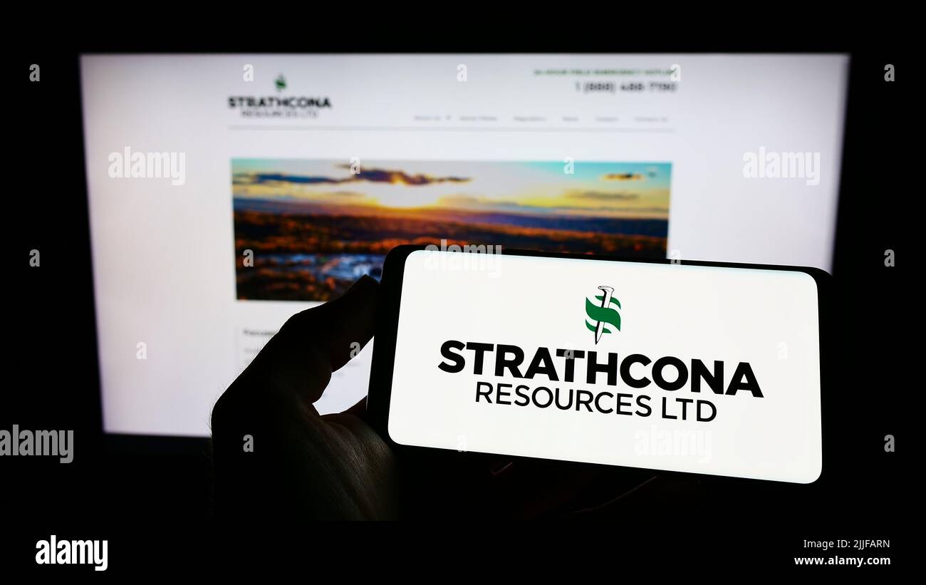 Persona che tiene il telefono cellulare con il logo della compagnia petrolifera canadese Strathcona Resources Ltd. Sullo schermo di fronte alla pagina web. Mettere a fuoco sul display del telefono. Foto Stock