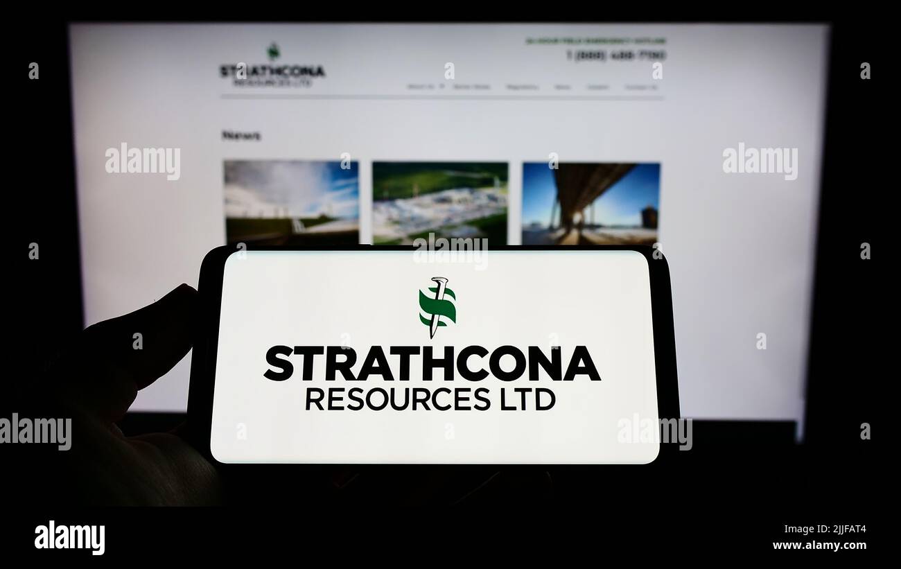 Persona che tiene il cellulare con il logo della compagnia petrolifera canadese Strathcona Resources Ltd. Sullo schermo di fronte al sito web. Mettere a fuoco sul display del telefono. Foto Stock