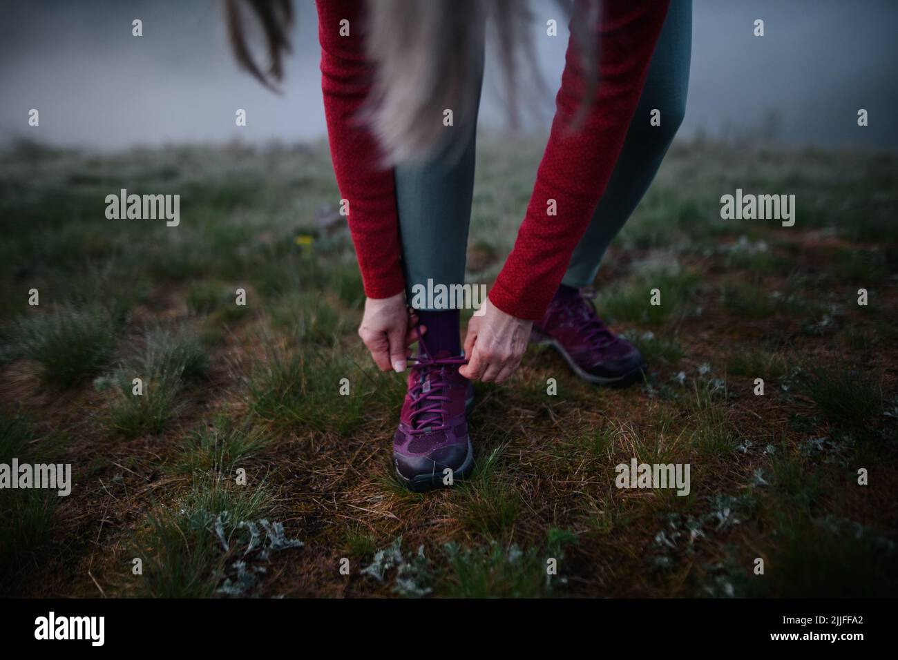 Primo piano di donna anziana che lega le sue scarpe prima di esercitare in natura al mattino presto con nebbia. Foto Stock