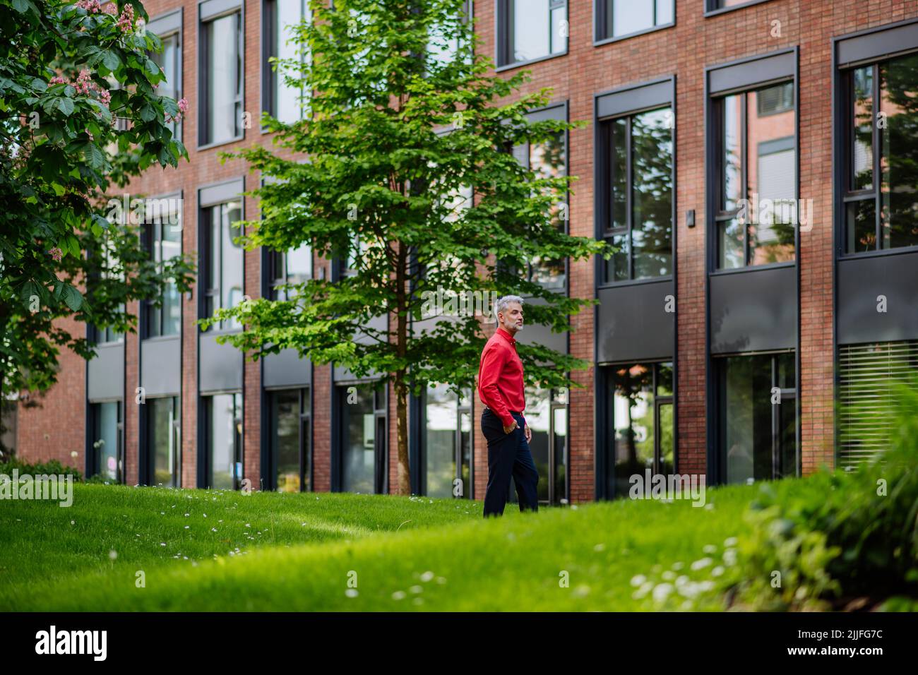 Uomo d'affari che cammina nel parco vicino ufficio edificio durante la pausa, concetto di equilibrio vita di lavoro. Foto Stock