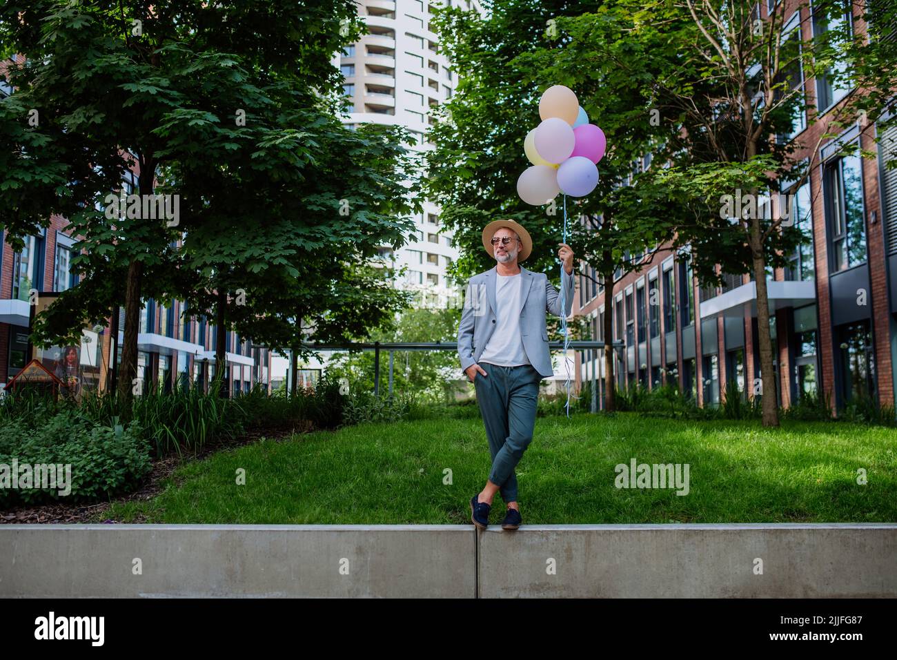 Ritratto divertente di uomo d'affari maturo felice energico tenendo palloncini e camminare sul muro, sentirsi liberi, lavoro vita equilibrio concetto. Foto Stock