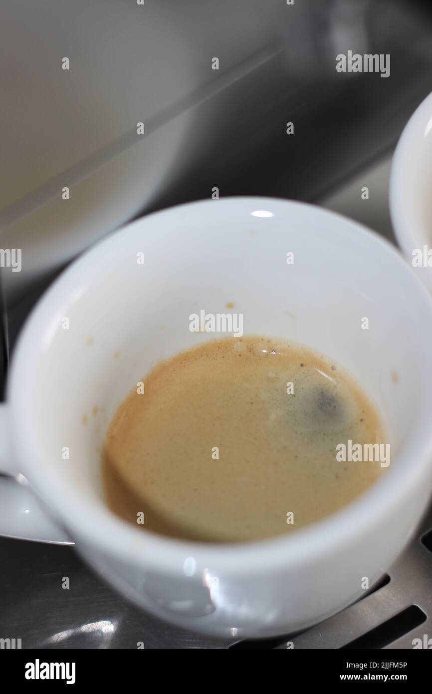 Espresso appena fatto in tazza piccola su fondo metallico. Preparazione del caffè mattutino a casa. Foto Stock
