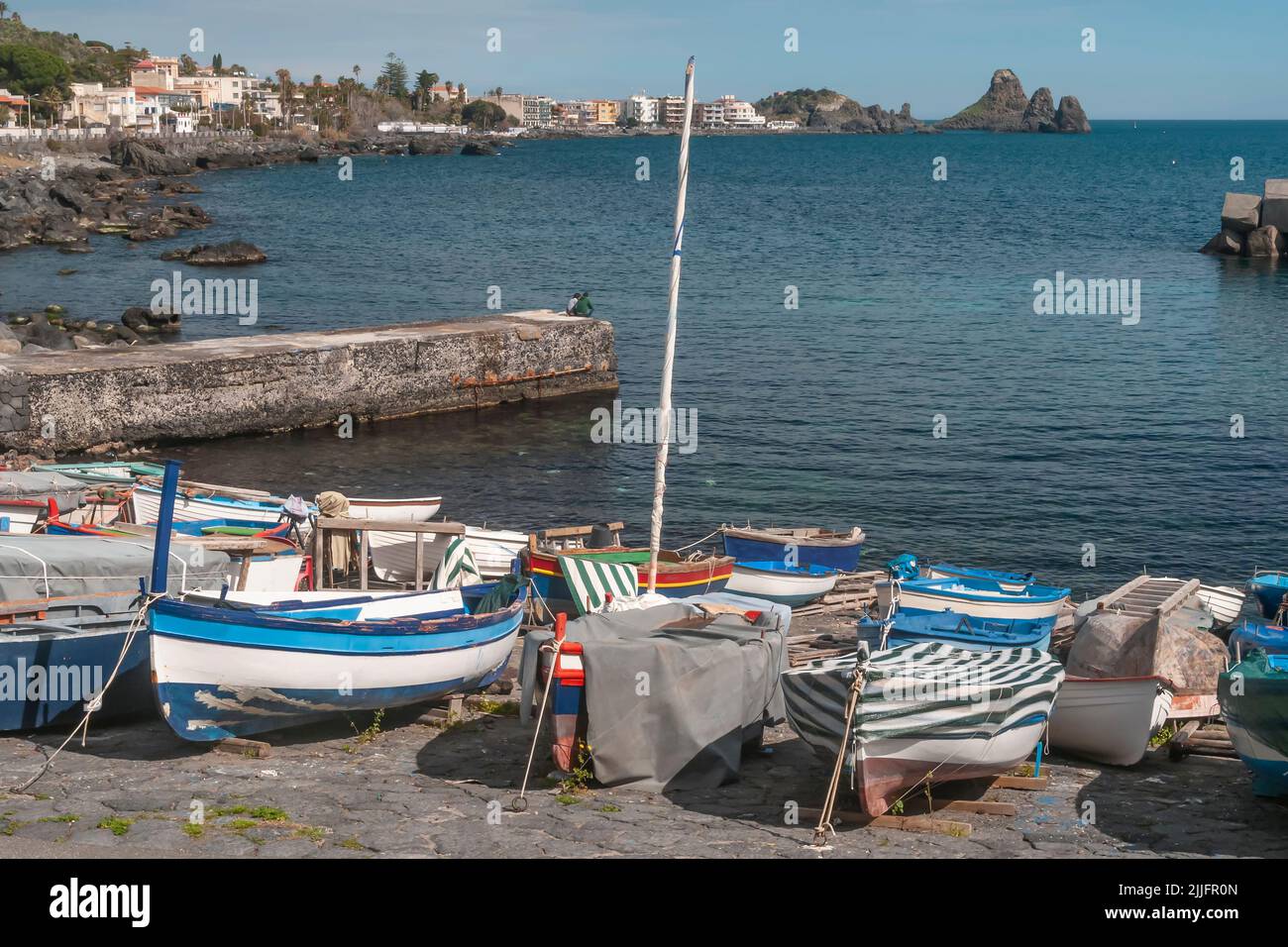 Vecchie barche in legno su una spiaggia di Aci Castello, con Aci Trezza sullo sfondo, Catania, Italia Foto Stock