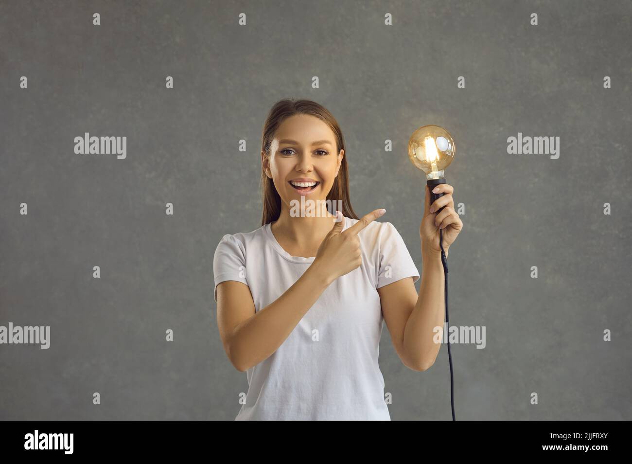 Allegra donna intelligente e intellettuale punta alla lampadina luminosa che tiene in mano. Foto Stock