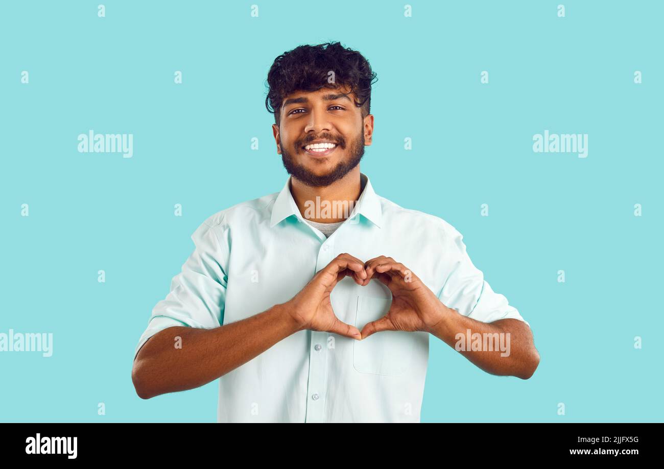 Ritratto di allegro e attraente ragazzo indiano che mostra gesto d'amore su sfondo azzurro chiaro. Foto Stock