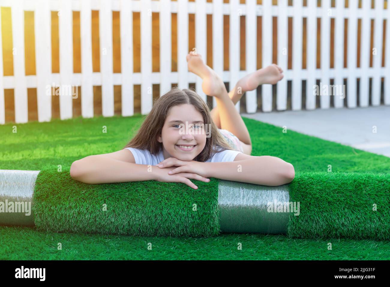 Sorridente giovane caucasica sdraiata sulla sua terrazza su un nuovo rotolo di erba sintetica. Bella erba artificiale pronta a posare Foto Stock