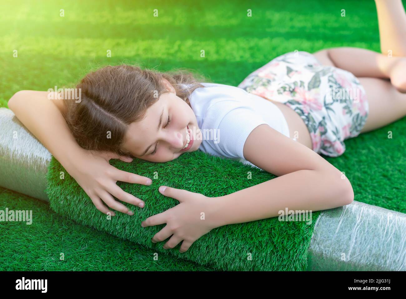 Sorridente giovane caucasica sdraiata su un nuovo rotolo di erba sintetica. Erba artificiale soffice e squishy pronta a deporre Foto Stock