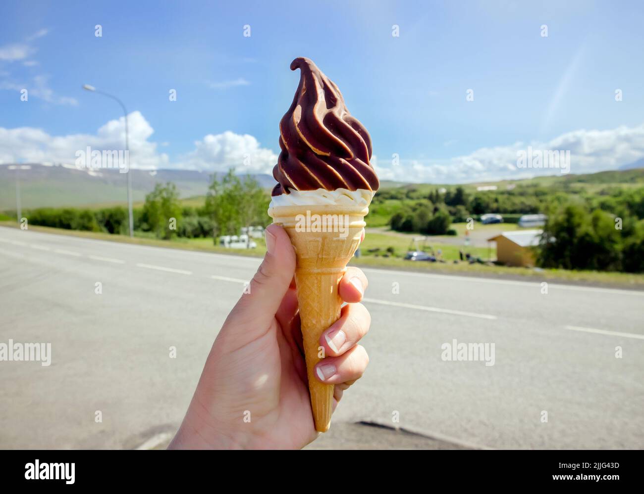 Tenuta di mano gustoso islandese locale soft serve gelato alla vaniglia immerso in cioccolata calda, Islanda natura sullo sfondo. Foto Stock