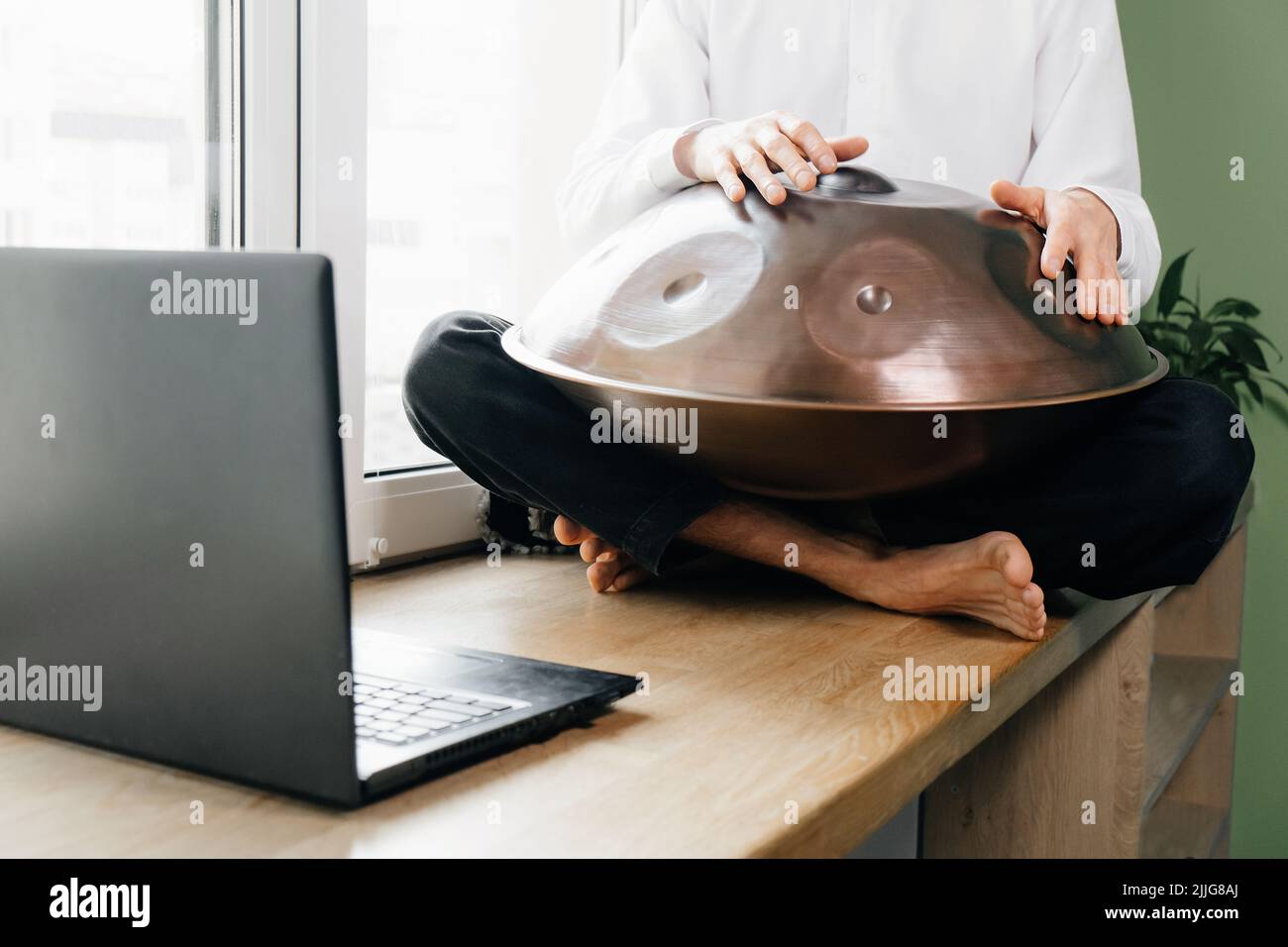 Uomo che suona su un tamburo appeso, o acciaio tamburo, Hangpan, moderno strumento di musica in acciaio a casa. Musica di meditazione per il relax. Impara a insegnare i corsi on-line su Foto Stock