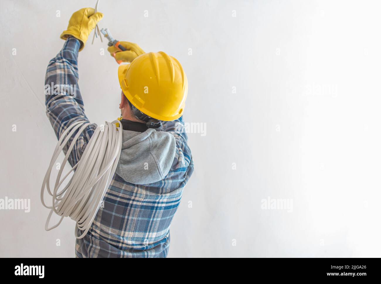 Elettricista professionista che indossa il cappello rigido giallo che fa l'illuminazione Installazione preparazione durante i lavori di ristrutturazione spelare i fili con dedicato Foto Stock