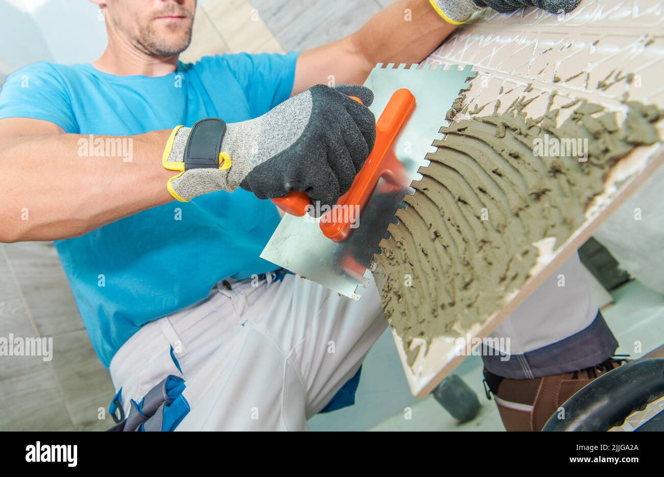 Lavoratore caucasico con cautela mettendo l'adesivo sulla piastrella utilizzando l'attrezzo speciale. Bagno in tema ristrutturazione e ristrutturazione. Foto Stock