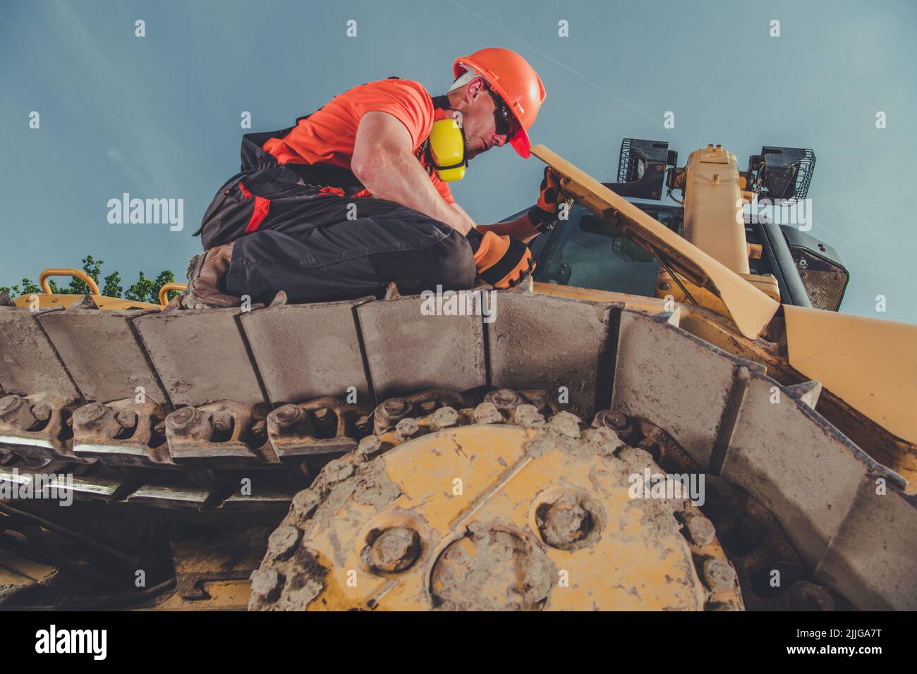 Lavoratore caucasico di costruzione maschile seduto sulla parte superiore del cingolo continuo della sua macchina per impieghi pesanti controllo della sua condizione prima di iniziare il lavoro. IO Foto Stock