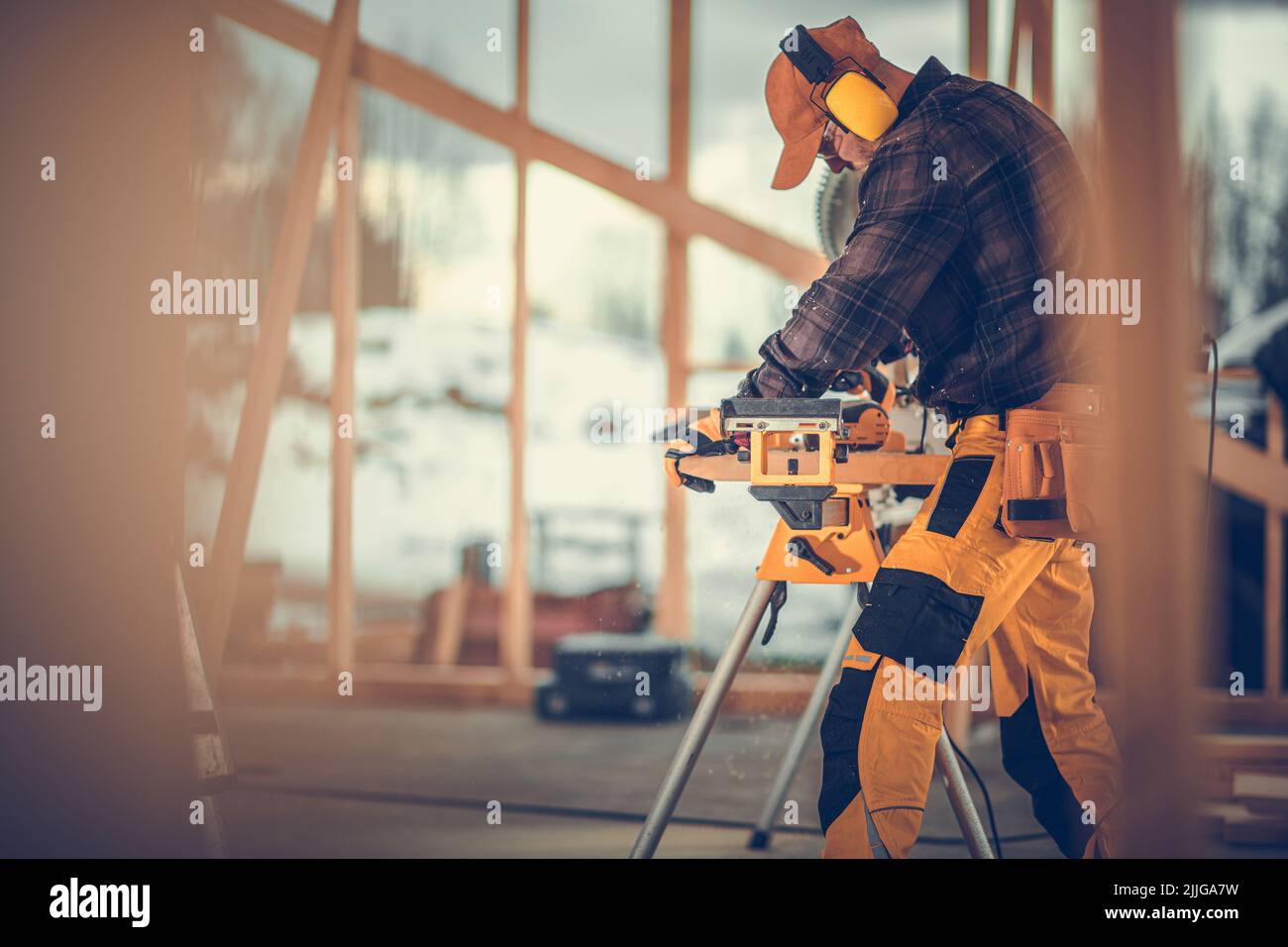 Professionista di costruzione che indossa le cuffie di riduzione di rumore che Planing la tavola di legno sul luogo di costruzione della struttura della casa di legno. Foto Stock